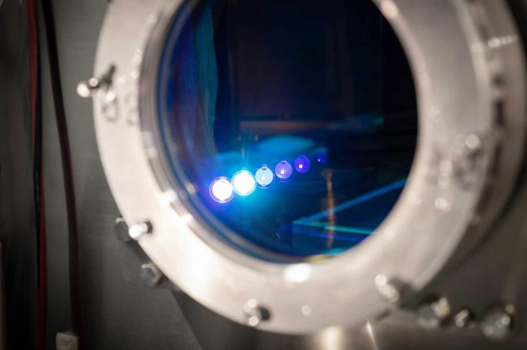 A close-up view of a vacuum chamber with several points of light in focus inside a circular window.