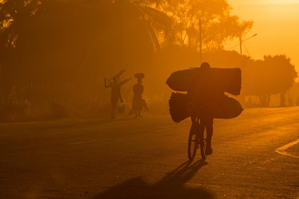 A yellowish haze creates a silhouette of a person on a bike carrying a heavy load.