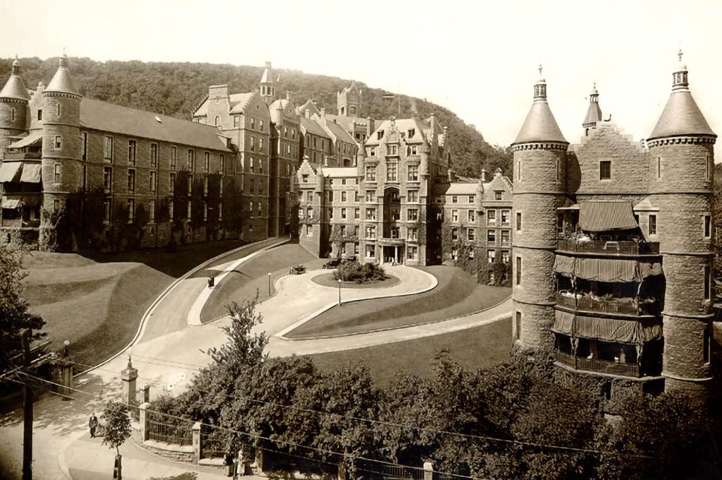 A grey and white photo of a multi-storeyed building with turrets at each corner and a large circular driveway in front.