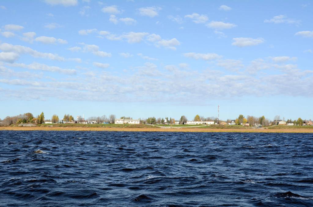 Low buildings and homes along a flat shoreline with water in the foreground. 
