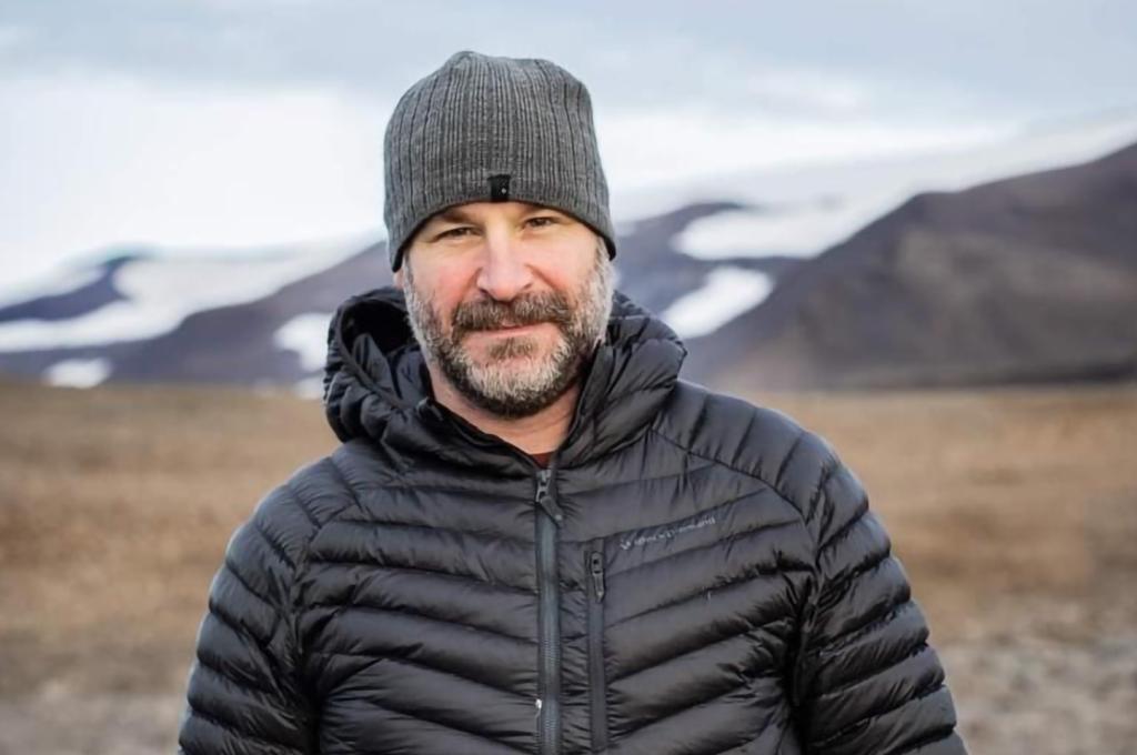 A person wearing a coat in an empty field, posing for a photo.