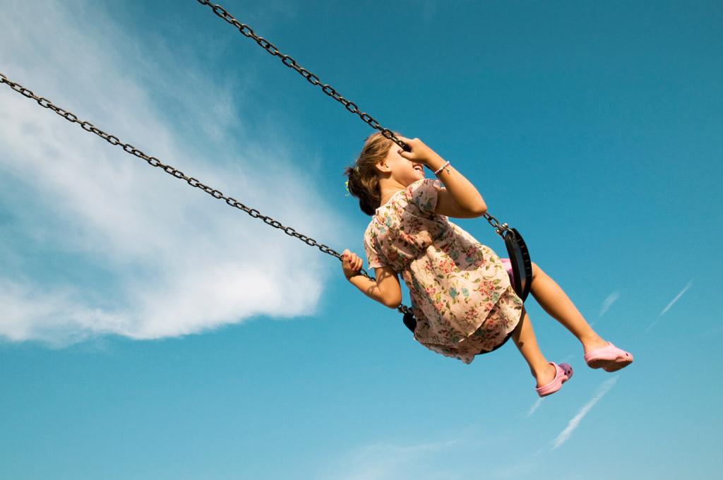 Prise de vue en contre-plongée d’un enfant sur une balançoire sur fond de ciel bleu.