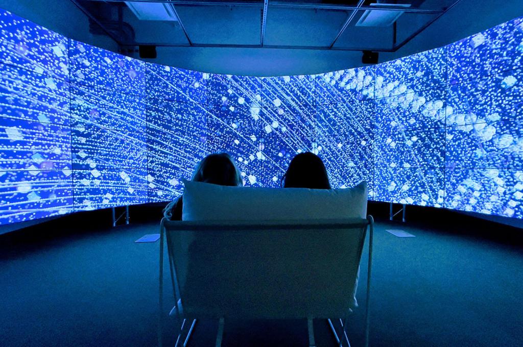 Deux personnes sont assises devant un mur vidéo incurvé qui affiche des rendus lumineux de satellites en orbite autour de la Terre.