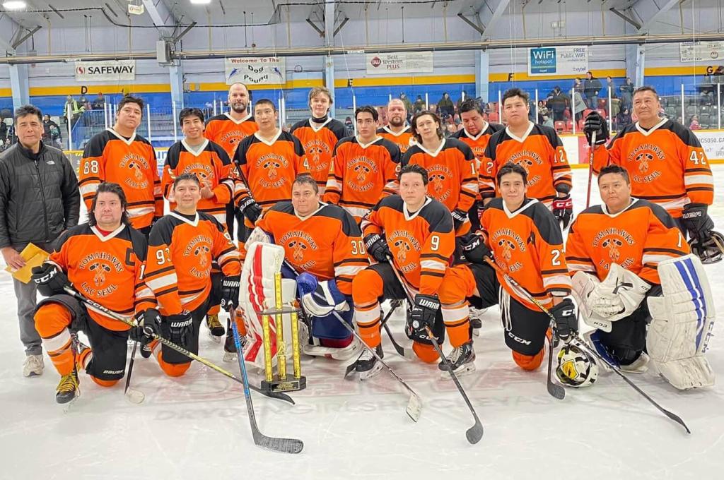 A hockey team in orange jerseys poses on the arena ice.