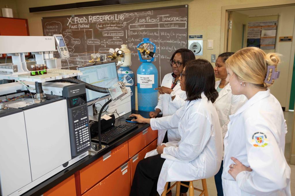 Quatre personnes sont réunies autour d’un spectromètre de masse posé sur une table de laboratoire.