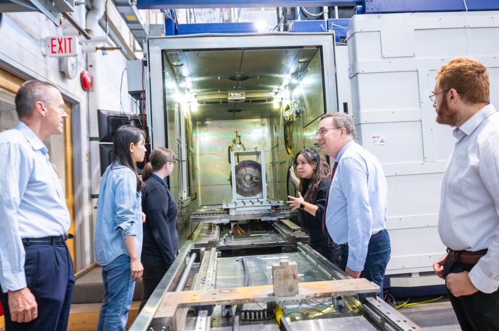 A group of people stand on either side of a long metal machine.