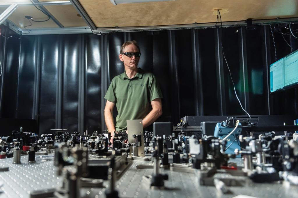 David Jones wears protective laser glasses as he stands behind a prototype on his lab bench.