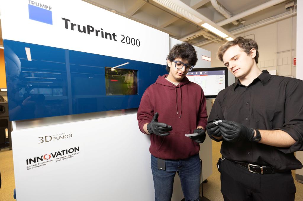 Deux personnes munies de gants de protection noirs et se tenant debout devant une grande machine TruPrint 2000 ont chacune dans les mains un petit objet métallique et semblent les examiner minutieusement.