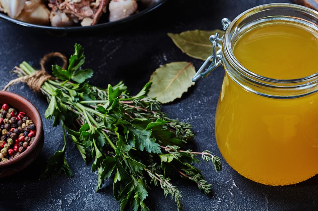 Un bocal de liquide jaune avec à côté, des herbes fraîches et un bol de grains de poivre
