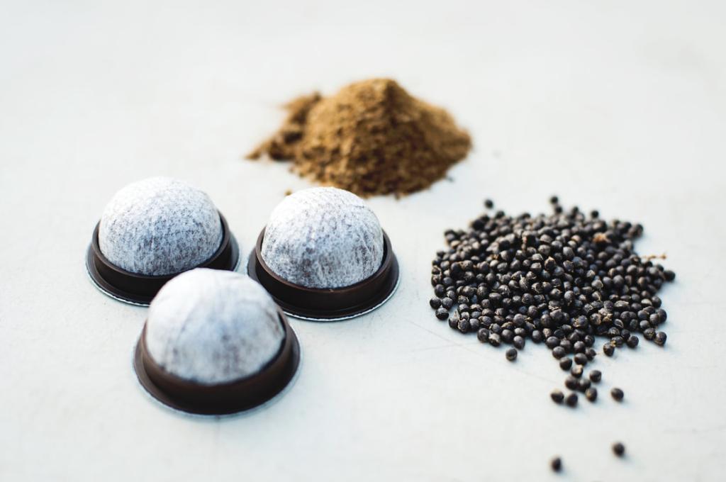 Three small piles of coffee beans, coffee grounds and coffee pods on a white background