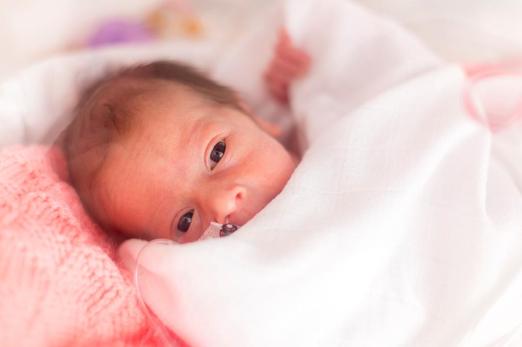 A tiny baby's dark eyes and nose peak out from the blanket she's swaddled in, her little fingers grip the edge.