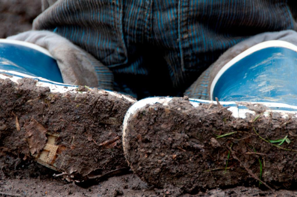 The soles of a child’s blue rubber boots, caked in mud