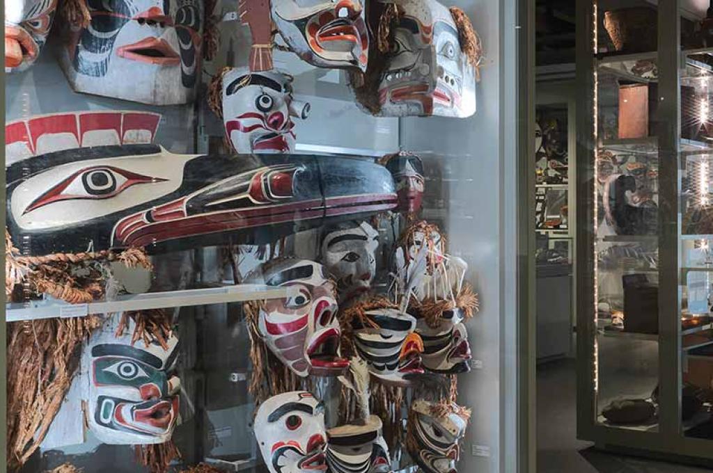 Une salle de musée peu éclairée compte de nombreux présentoirs affichant des masques autochtones peints de couleurs vives.