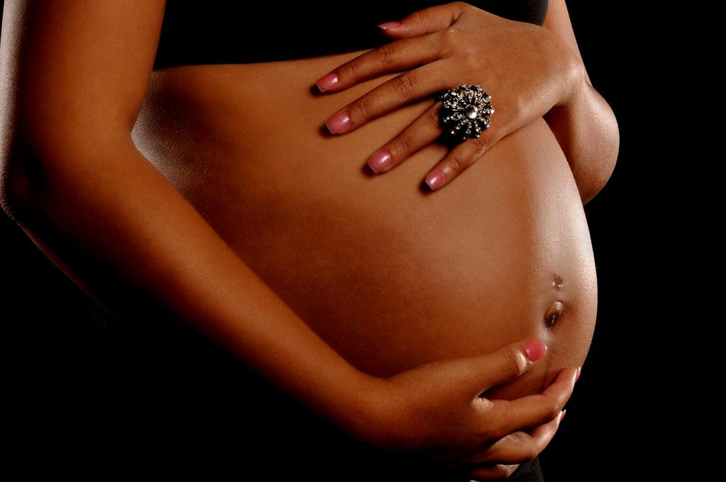 A close up shot of a woman’s hands on her pregnant stomach. 