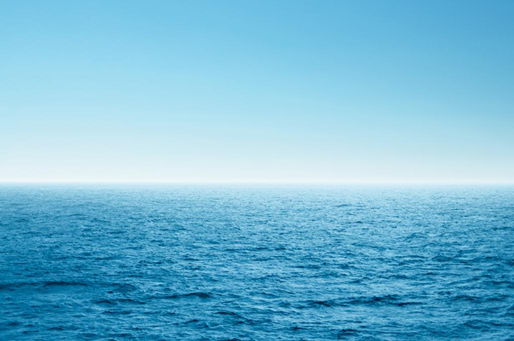 A thin white line on the horizon separates a wide expanse of blue ocean from a blue sky