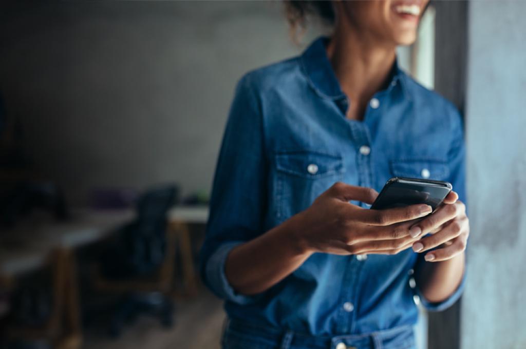 A woman, who is blurred out in the background, holds a mobile phone in the foreground