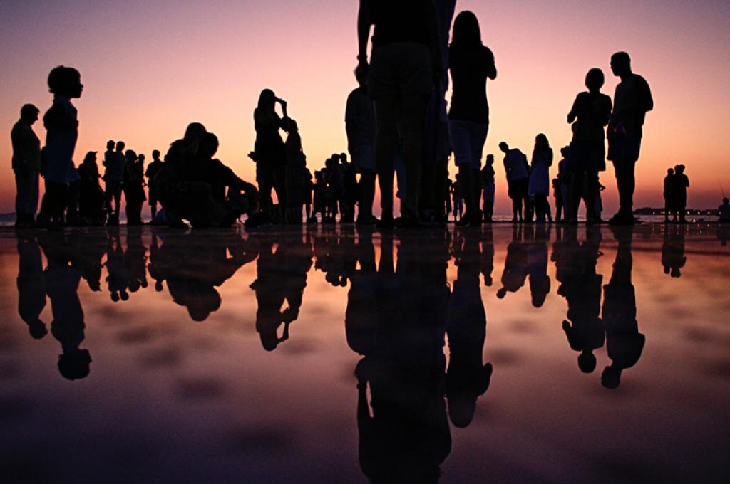 Silhouettes of many people interacting on a reflective surface that looks like water.