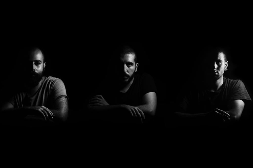 Three men with crossed arms sit in shadow