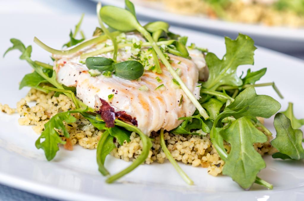 A plate of cooked sea bass fillet on a bed of arugula and couscous
