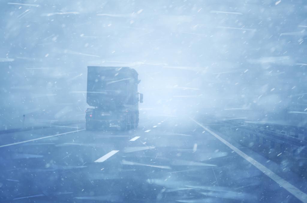 A transport truck on a snow-covered road in a blizzard.