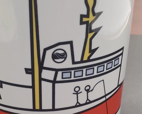 Tasse blanche arborant un dessin d’enfant représentant un bateau stylisé rouge et jaune.