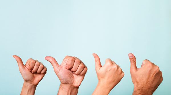 A stock photo of four hands in a row giving a thumbs up against a grey background.