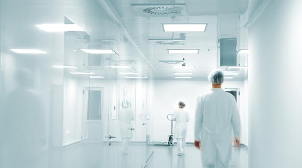 Photo de banque d’images montrant un corridor d’hôpital blanc avec deux travailleurs de la santé non identifiables en blouse blanche qui marchent dos à l’objectif.