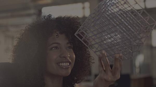 A faded stock photo of a woman holding up a white, wire cube and smiling at it.