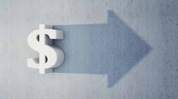 A stock illustration of a white bold dollar symbol hanging up on a grey wall with a shadow of an arrow behind it, pointing to the right.