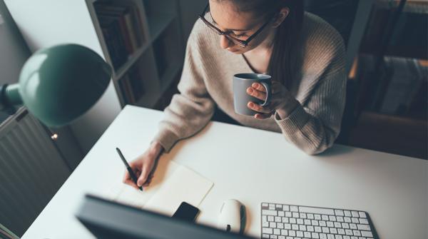 Photo d'une femme assise à un bureau, écrivant sur un bloc-notes et vue en contre-plongée .