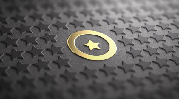 A stock image of a gold star in the middle of a gold ring on a black surface that takes up the whole image imprinted with rows of black stars.