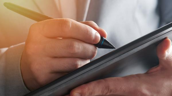 A close up photo of a person holding an electronic pad in one hand and a pen in the other.