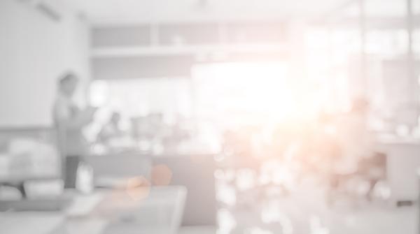 A blurred photo of a bright, white office space with floor to ceiling windows and the sun shining through.