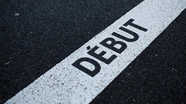 Gros plan d’une ligne de départ sur une piste de course. La piste est noire et la ligne de départ est blanche. Le mot «DÉBUT» y est imprimé en noir au pochoir.